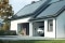 Auf dem Foto sehen Sie ein Haus mit einer Photovoltaikanlage auf dem Dach und einem Ladegerät für Elektroautos an der Wand. 